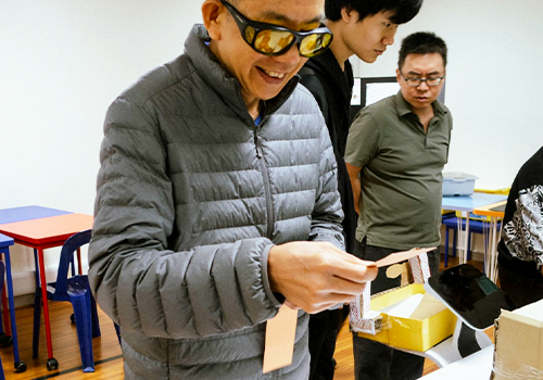 A mentor with visual impairment assessing a student prototype during Journey Bright.